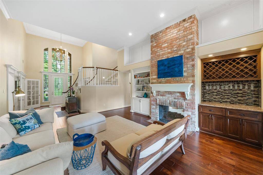 This spacious living room features high ceilings, and elegant hardwood floors. It includes built-in shelves, a wine rack, dry bar and a cozy seating area. Natural light streams through tall windows, enhancing the open, airy feel.