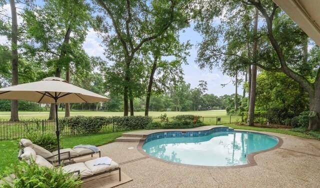This backyard features a serene pool surrounded by lush greenery and mature trees, with a view of a golf course. Relaxation spots include lounge chairs and an umbrella, perfect for enjoying the tranquil setting.