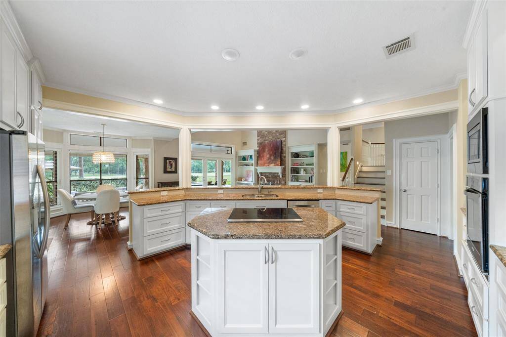 This spacious kitchen features a central island with a cooktop, sleek granite countertops, and ample cabinetry. It's an open-concept space with hardwood floors, recessed lighting, and views into the dining and living areas.