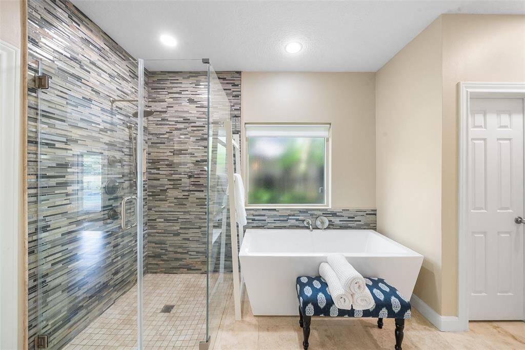 This modern bathroom features a sleek glass-enclosed shower with stylish tilework, a spacious soaking tub, and a bright window for natural light. The neutral tones and elegant design create a relaxing atmosphere.