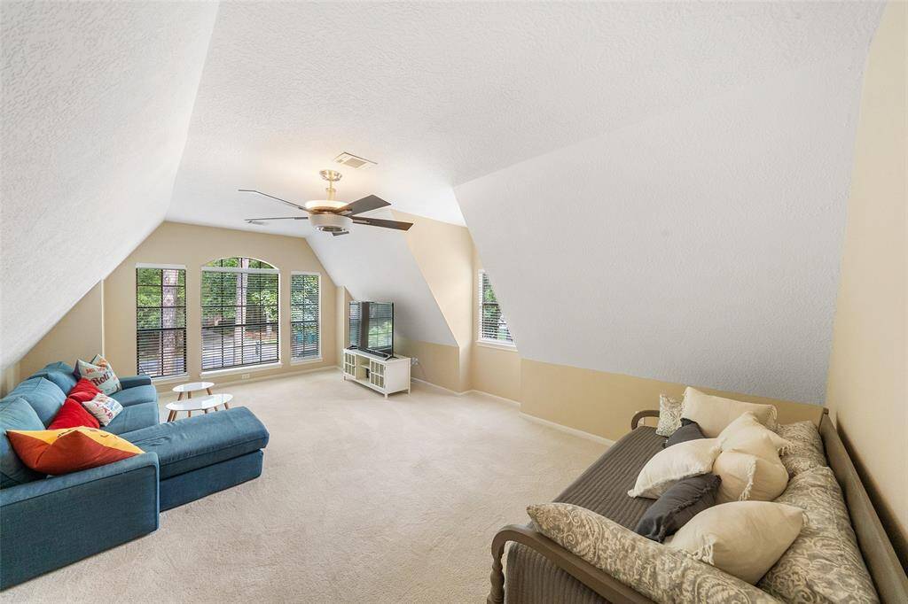 Bright and spacious game room with angled ceilings, featuring large windows for natural light, a cozy seating area, and neutral carpeting. Ideal for a family room or play area.