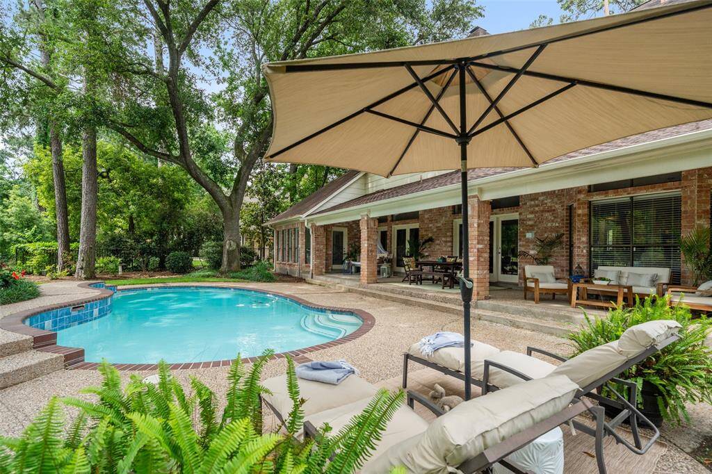 This backyard features a serene pool surrounded by lush greenery and mature trees, with a view of a golf course. Relaxation spots include lounge chairs and an umbrella, perfect for enjoying the tranquil setting.
