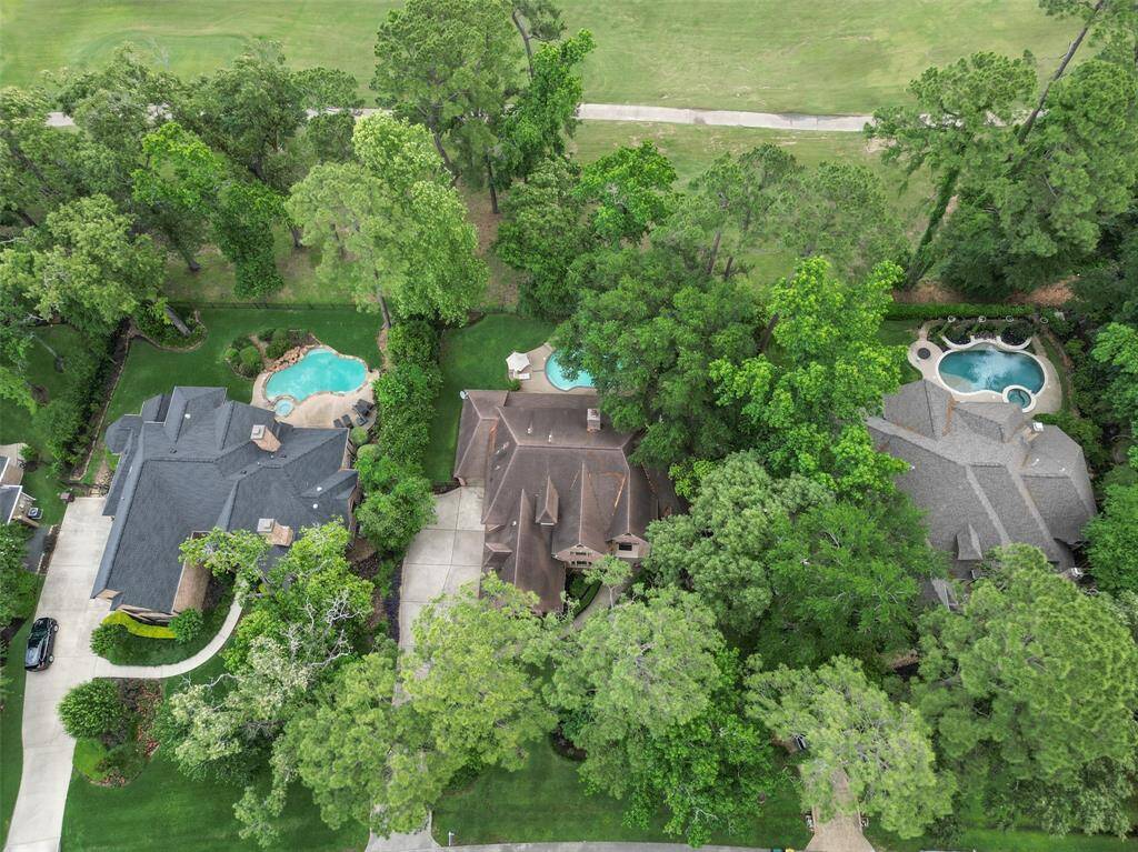 Aerial view of a lush neighborhood with three large homes, each featuring a private pool. Surrounded by mature trees, the properties offer privacy and a serene setting. Nearby green space enhances the tranquil atmosphere.