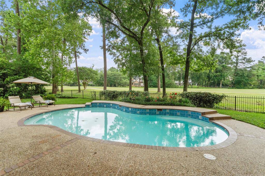 Golf course view backyard features a charming pool with a stone surround, set against a backdrop of lush greenery and a well-manicured lawn, offering a serene and private outdoor retreat.