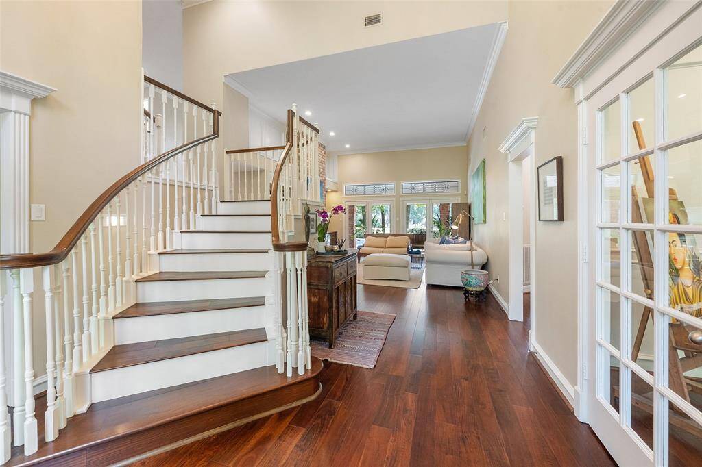 This inviting home features a spacious, open foyer with elegant hardwood flooring and a grand, curved staircase. Natural light floods the area, leading into a cozy living room with large windows and modern furnishings, creating a warm and welcoming atmosphere.