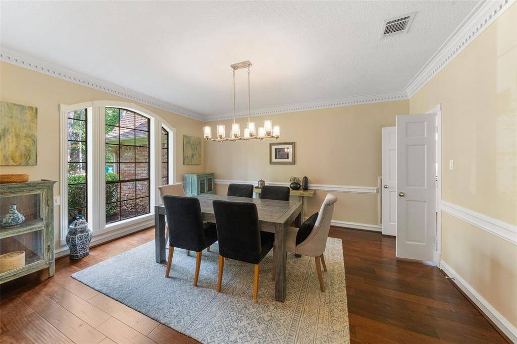 Elegant dining room with hardwood floors, crown molding, and large windows. Features a modern chandelier, and neutral decor, creating a warm, inviting atmosphere.