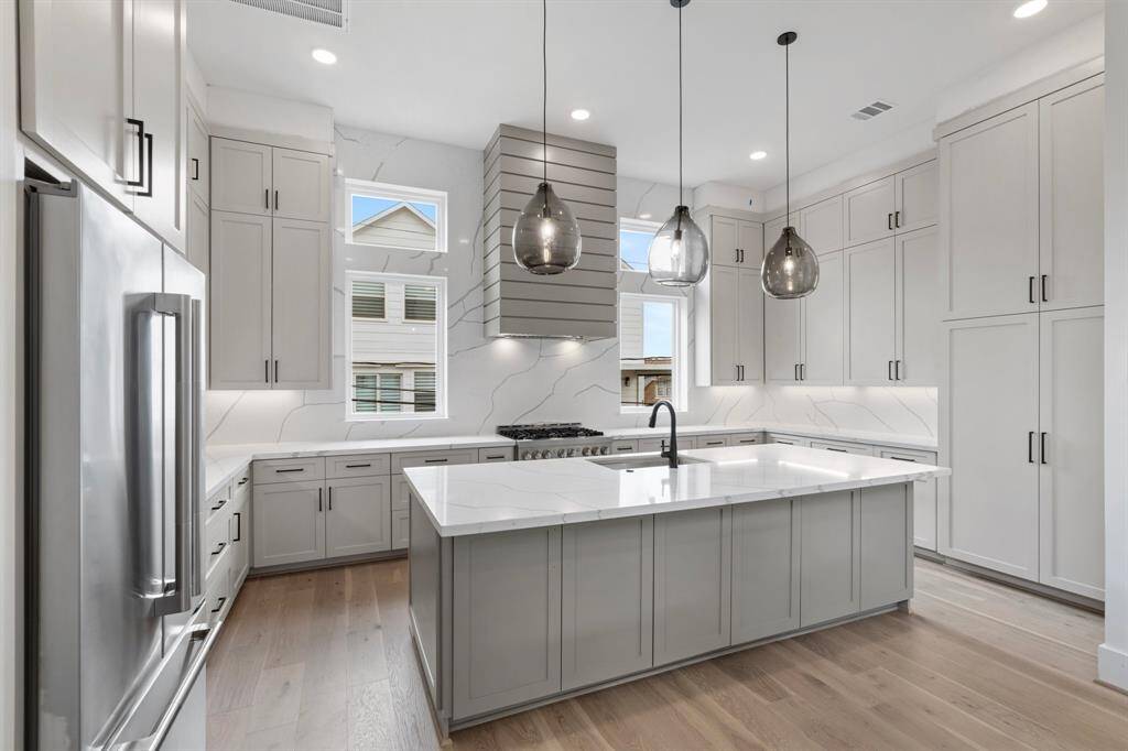 Another view of this stunning kitchen equipped w/ ample storage w/ custom-built cabinets that go to the ceiling and large double door pantry.  Custom touches w/ pull-out spice racks and cookie tray divider. Natural light floods in through two large windows, beautifully complemented by Visual Comfort pendants and recessed lighting.