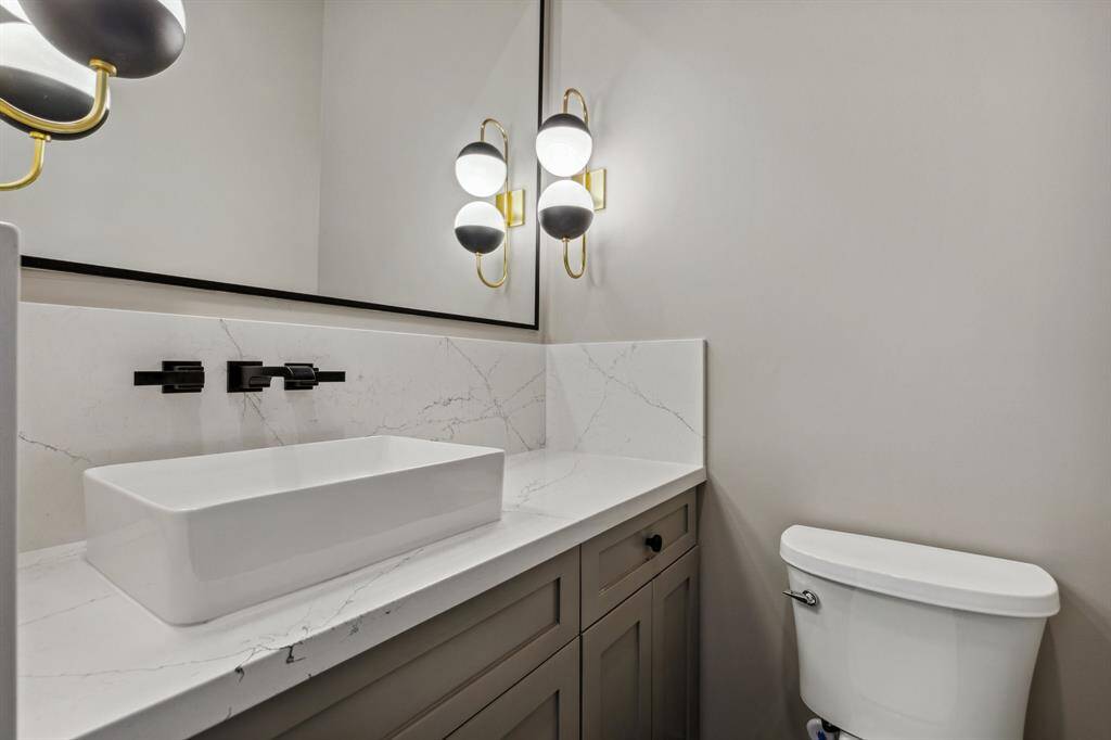The gorgeous powder room features art deco-inspired tile flooring (not shown), an overmount vessel sink with wall-mounted faucet, and a custom-built vanity. Framed mirror and twin Visual Comfort sconces complete this chic, statement-making space.