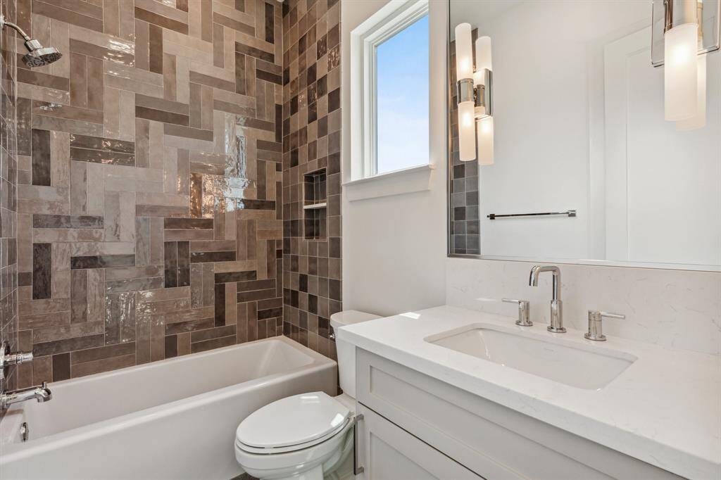 This stylish ensuite bathroom for secondary bedroom #1 on the 3rd floor, features sleek 24x48 porcelain tile floors, a custom-built vanity with pull-out shelves, quartz countertop, and Top Knob hardware. Enjoy the spacious walk-in closet with dresser, while the tub/shower combo with decorative tile wall adds a touch of elegance. Visual Comfort sconces and a Kohler toilet complete the refined space.