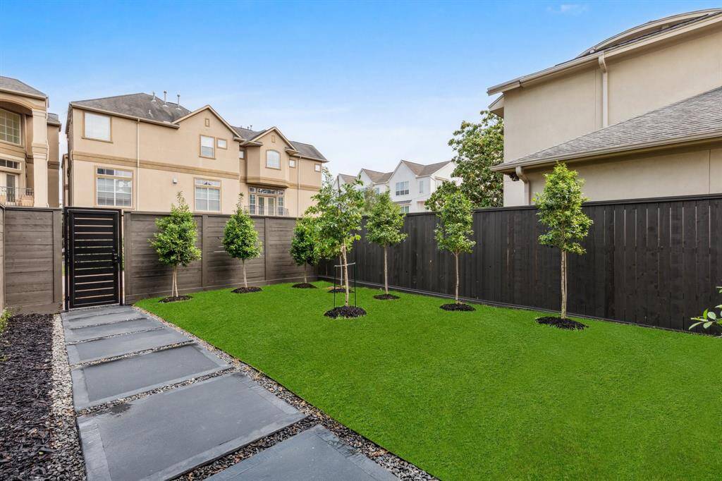 Another view of the spacious yard, now framed by a brand-new cedar wood fence and a custom iron front door. A colored concrete walkway adds curb appeal as it leads you to the elegant entry. Note: grass has been edited.