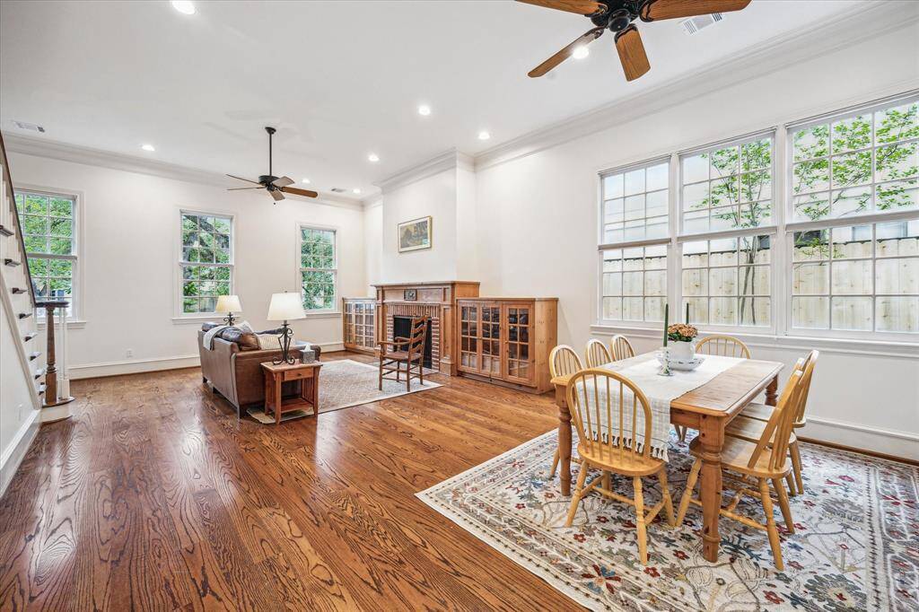 This light-filled living and casual dining space is enhanced by soaring ceilings, timeless wood flooring, and a wall of expansive windows that invite the outdoors in. A stately fireplace framed by built-in cabinetry adds warmth and charm, creating a welcoming atmosphere perfect for relaxed gatherings.