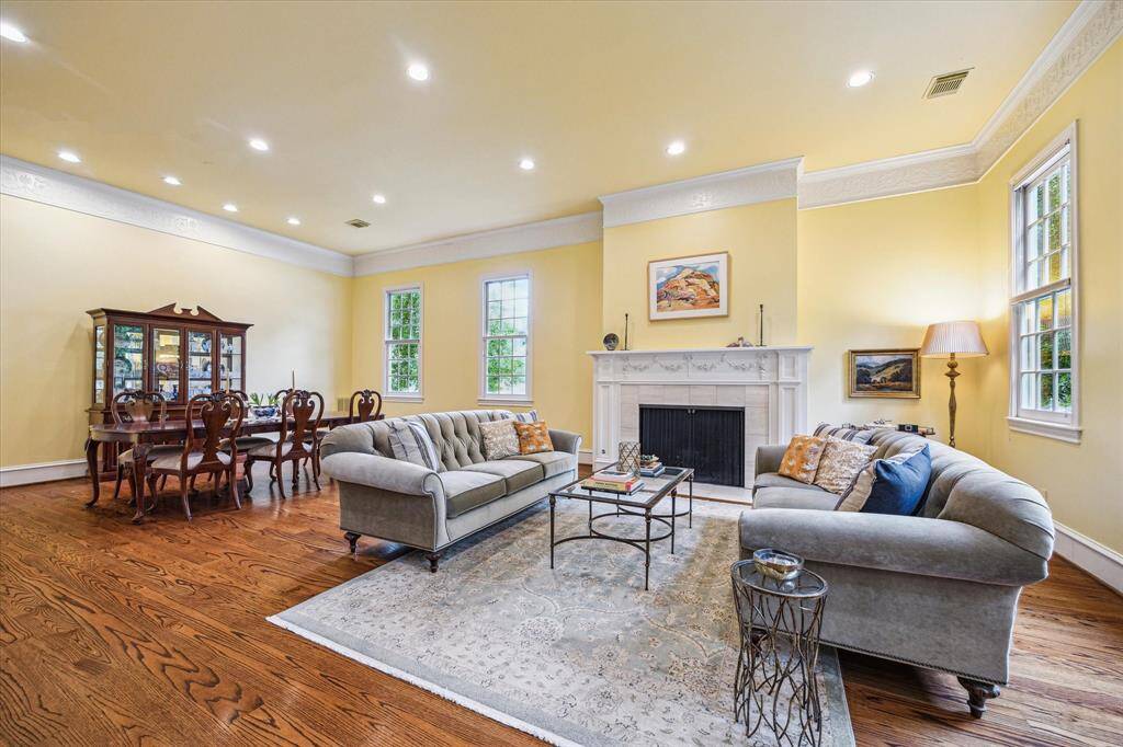The family room radiates warmth with its soft yellow walls, intricate crown molding, and a beautifully detailed fireplace that serves as a stunning focal point. Large windows flood the space with natural light, creating an inviting setting for everyday comfort or elegant entertaining.