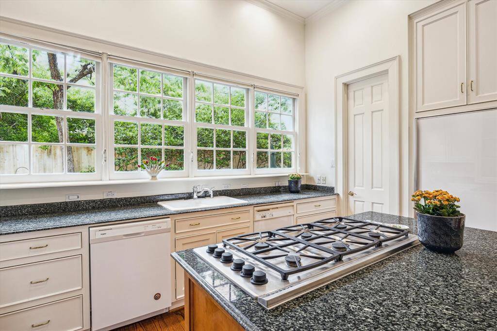 Sunlight pours through a wall of windows in this beautifully appointed kitchen, highlighting granite countertops, classic white cabinetry, and a central gas cooktop island perfect for culinary creativity.
