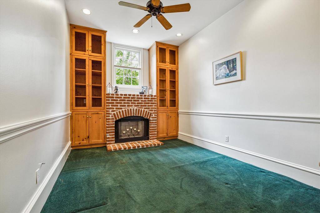 This charming home office features custom built-ins flanking a rustic brick fireplace, with crown molding, natural light, and timeless character creating an inspiring workspace.