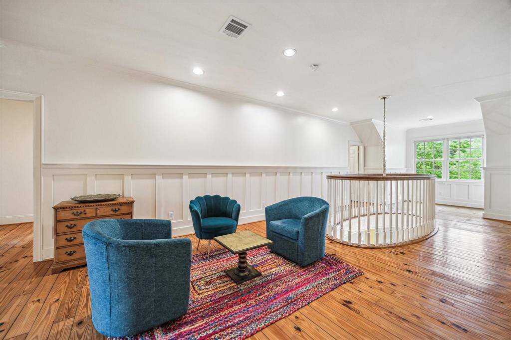 The upstairs landing offers a bright and inviting sitting area with charming wide-plank flooring, classic wainscoting, and a striking view over the dramatic circular stairwell.