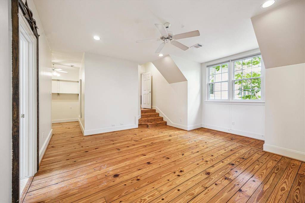 This spacious upstairs secondary bedroom features charming dormer angles, wide-plank wood flooring, and a large window that fills the space with natural light.