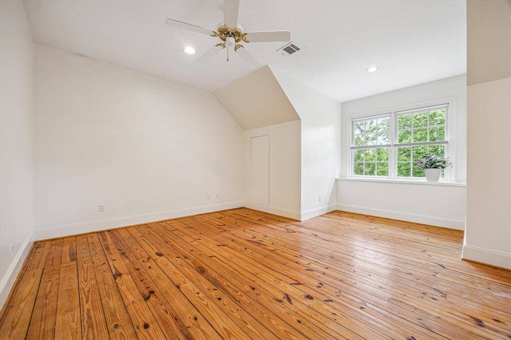 This bright secondary bedroom features wide-plank pine floors, a charming dormer nook, and a large window that frames lush treetop views.