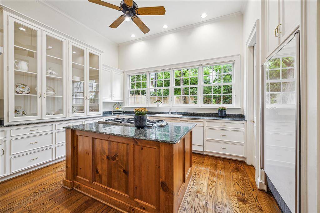 A rich wood-paneled island topped with sleek granite anchors this bright, airy kitchen, perfectly complementing the crisp white cabinetry and expansive garden-view windows.