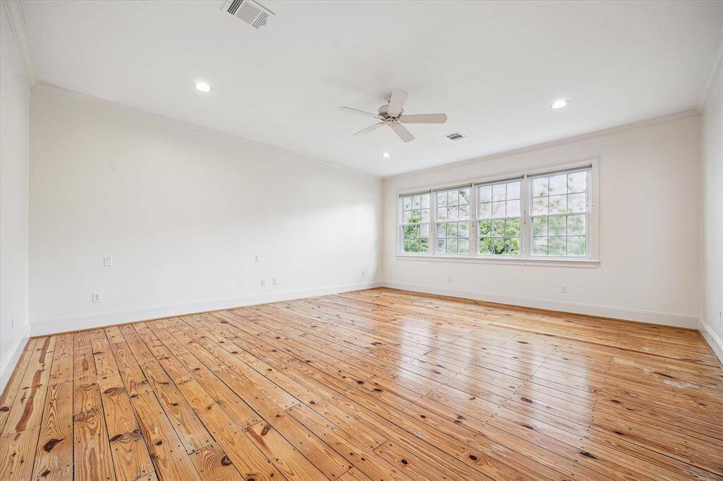 The expansive primary retreat features wide-plank pine flooring, soft natural light from a wall of windows, and a serene, minimalist aesthetic perfect for rest and relaxation.