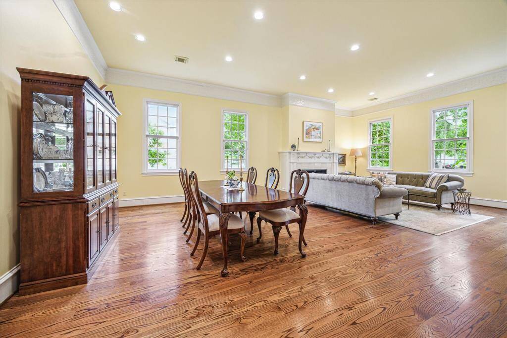 Bathed in natural light, the formal living and dining rooms exude warmth with rich wood floors, elegant crown molding, and large windows that frame the serene outdoors. A stately fireplace anchors the space, creating a refined yet inviting setting for entertaining.