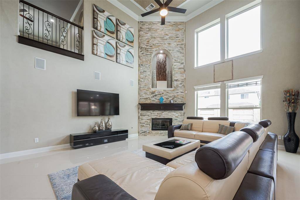 This spacious living room features high ceilings and large windows for ample natural light. It includes a modern stone fireplace and elegant decor. The open layout creates an inviting atmosphere, perfect for relaxation and entertaining.