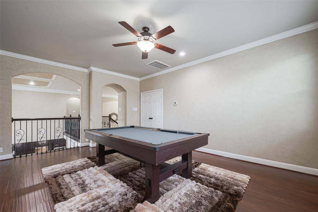 Game room features a modern pool table, elegant wood flooring, and a ceiling fan. It opens up to a hallway with decorative arches and iron railings, offering a sophisticated and inviting entertainment space. The Media room is to the right of this game room