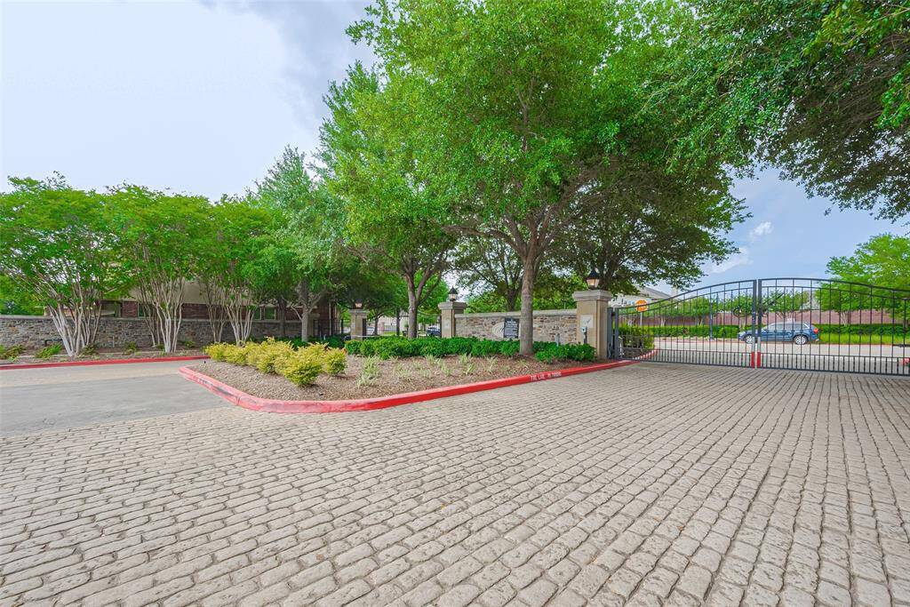 This photo shows a gated entrance to a residential community, featuring a paved driveway, lush trees, and well-maintained landscaping, offering a sense of security and privacy.