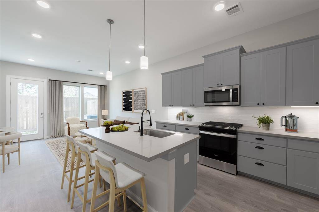 Kitchen has quartz seating island, staineless appliances incuding gas range, cabinet and pot drawers and pendant lighting. (virtually staged)