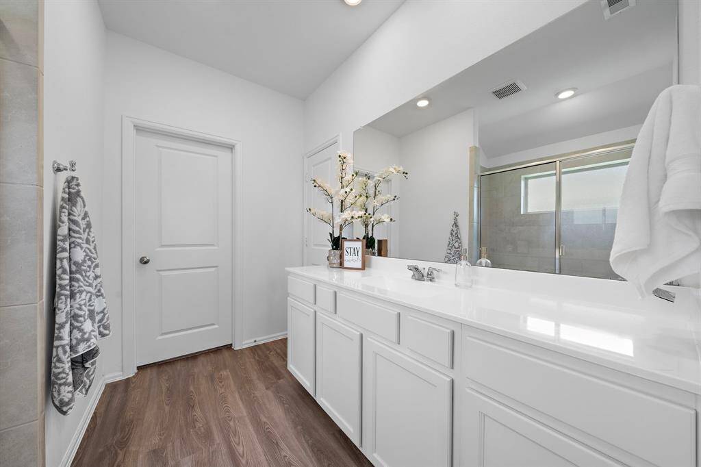 Bright and spacious, the bathroom features a large vanity, a glass-enclosed shower, and an oversized walk-in closet, offering a modern and clean aesthetic.