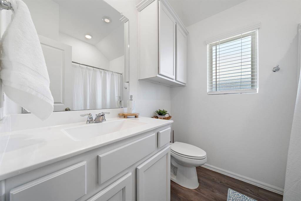 The secondary bathroom is bright and airy, featuring a modern vanity with ample storage, a sleek countertop, and a large mirror. It has a shower-tub combo with a curtain and a window that allows natural light.