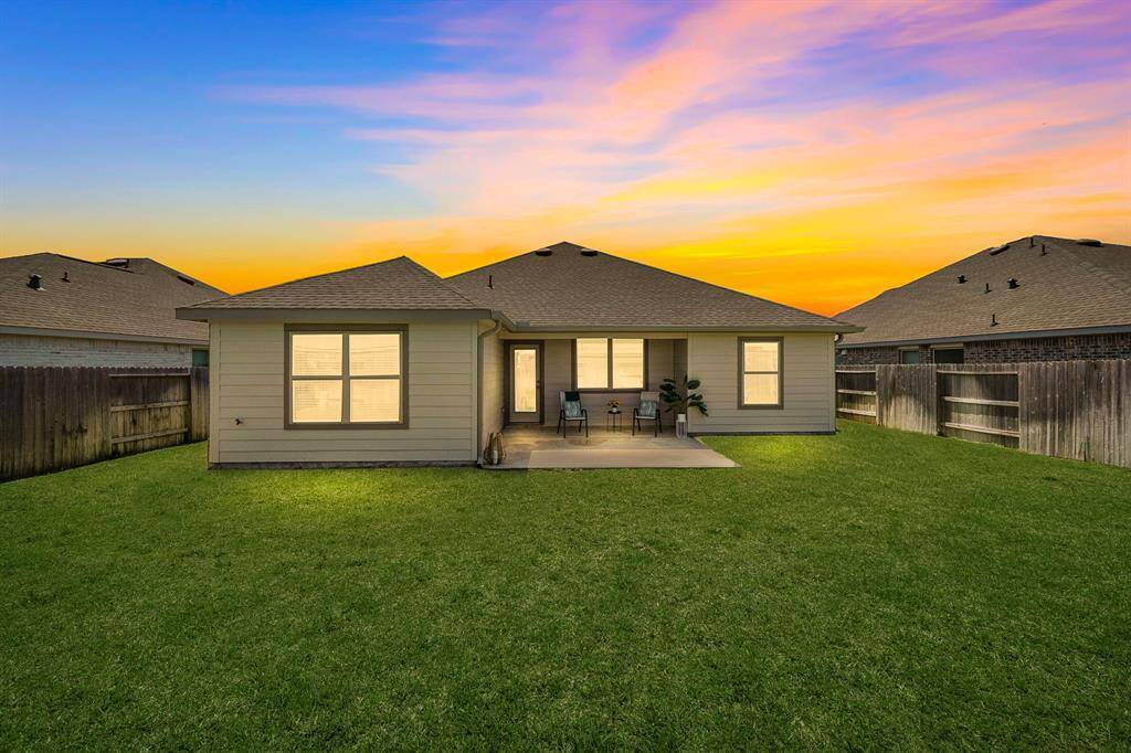 The house features a well-maintained lawn, a cozy patio area with seating, and a privacy fence, offering a serene outdoor space.