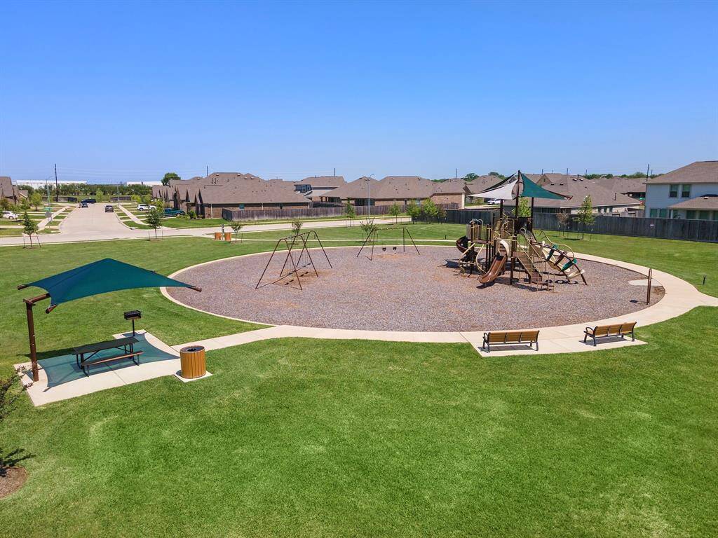 A spacious community playground with swings, benches, and a shaded picnic area.