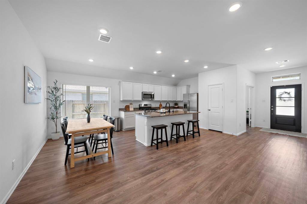 The house offers a bright, open-concept kitchen and dining area with modern fixtures. It features a spacious kitchen island with bar seating and stainless steel appliances. The dining area is well-lit with natural light from large windows, creating an inviting and functional space.