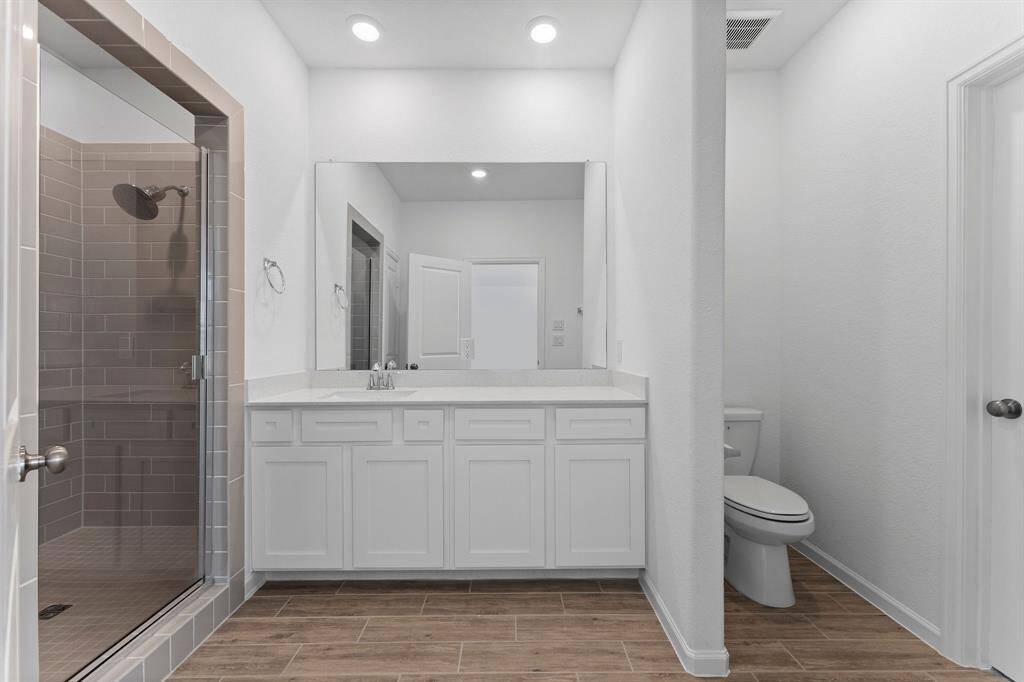 The owner’s en suite is a calming sanctuary, designed to evoke instant tranquility the moment you step inside. Thoughtful features include wood-look tile flooring, a spacious walk-in shower, an extended quartz countertop with sink, a private commode area, a generous linen closet, and soft recessed lighting—all combining to create a spa-like retreat.