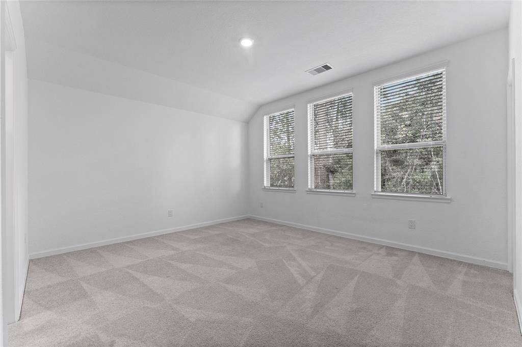 A secondary bedroom offers lush carpeting, sloped ceiling, large walk-in closet with sunny window, ceiling light, and three sunny windows with blinds and restful wooded back yard views. It has direct access to a Hollywood bath shared with Bedroom 3.