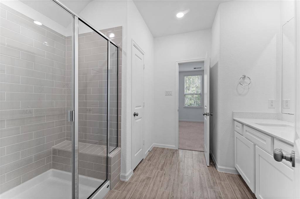 2nd full Hollywood bathroom for Bedrooms 2 and 3 includes wood-look tile flooring, single sink, quartz countertop, linen closet, toilet, and rectangular-tiled shower with built-in toiletry shelves, bench seat, and large rainfall showerhead.