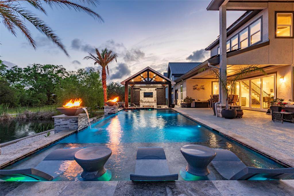 Step outside to an unforgettable backyard oasis showcasing a stunning infinity-edge pool with ambient lighting, built-in loungers and tables, a swim-up bar, two elegant fireplace features, and a covered sunken patio/outdoor kitchen area—designed for ultimate relaxation and entertaining.