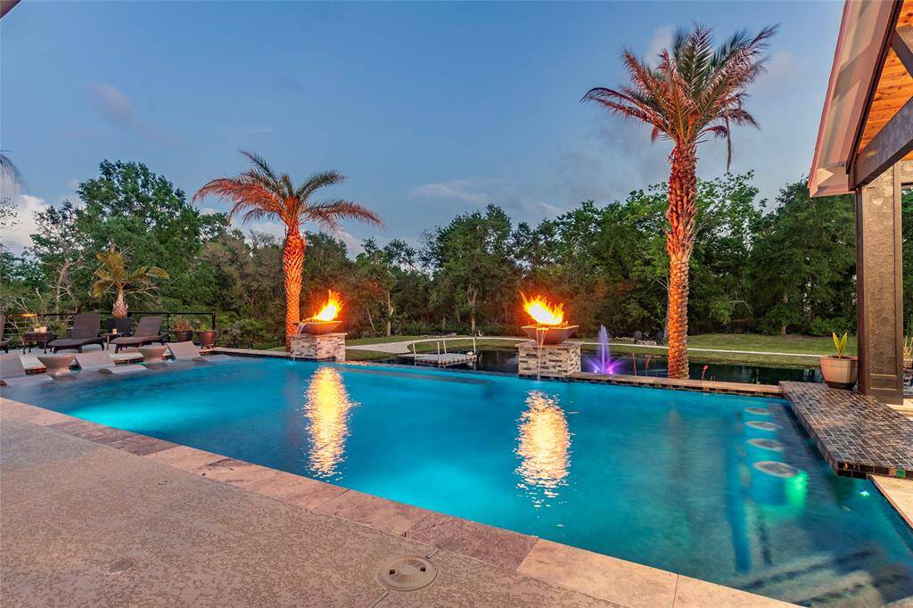 Showstopping infinity-edge pool features a glass tile swim-up bar with four built-in underwater bar stools—perfect for effortless gatherings. Overlooking a serene, stocked pond with a lighted fountain, walking trail and surrounded by mature trees, this private, resort-style oasis offers unparalleled tranquility and sophistication.