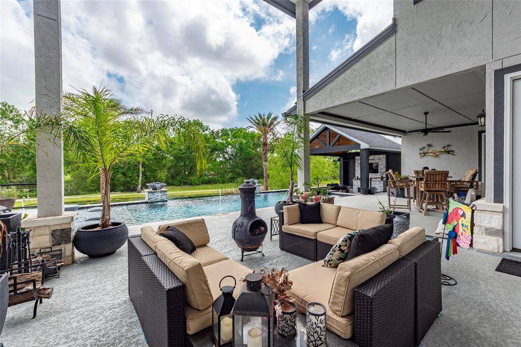 Expansive covered outdoor living and patio areas seamlessly opens to the family room through expansive sliding glass doors, showcasing Cool Deck, soaring ceilings, and elegant column accents—all overlooking the dramatic infinity-edge pool and serene pond for a truly immersive outdoor experience.