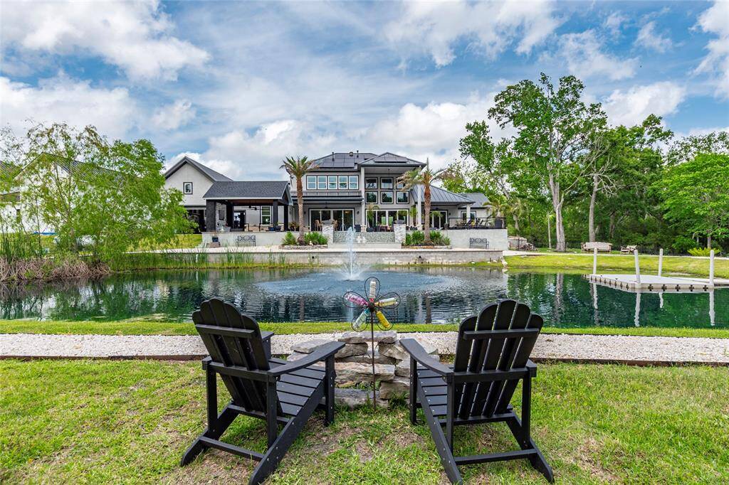 Another captivating view of the expansive, fully stocked pond and dock area, framed by a scenic walking trail and lush landscaping. The entire property is securely enclosed with elegant exterior metal fencing, including a dedicated side yard for pets. Peace of mind comes standard with a comprehensive security system and 10 strategically placed exterior cameras. A full irrigation system ensures effortless maintenance of the professionally designed grounds, while discreet, paid-in-full solar panels on the rea