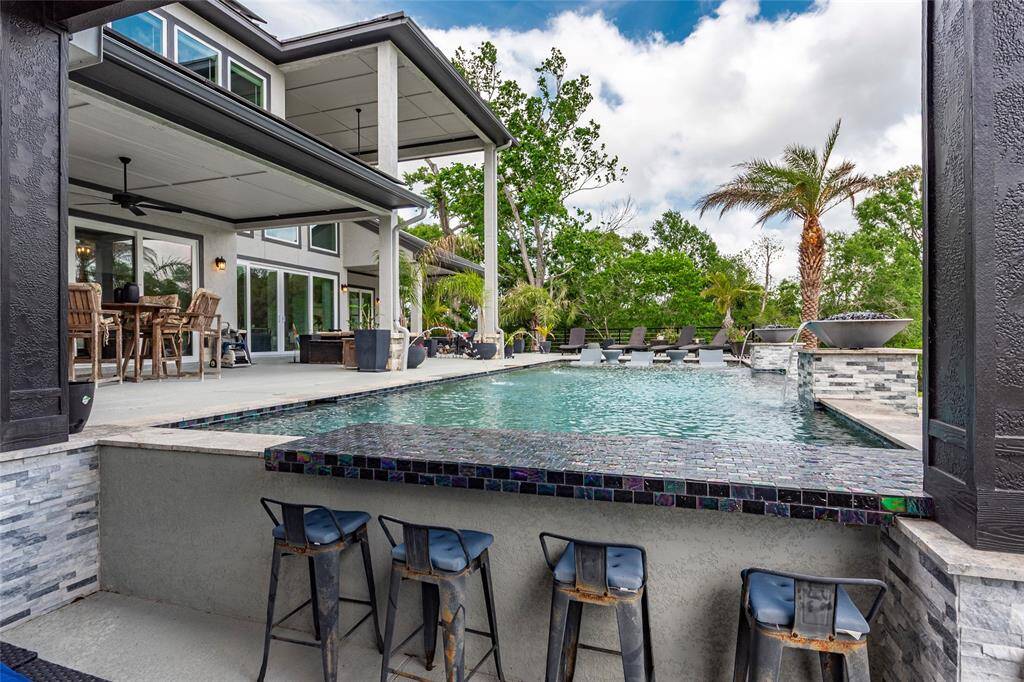 This elegant open-air retreat seamlessly blends comfort and design—perfect for upscale gatherings. Entertain in style in the stunning 18' x 17' sunken outdoor kitchen with serving bar which doubles as swim-up bar, boasting soaring 10' ceilings, a built-in TV, and a striking 9' x 6' ventless glass fireplace.