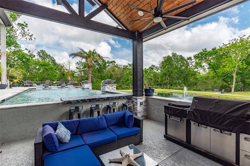Enjoy dual-sided seating at the glass-tiled swim-up bar, perfectly nestled beneath the outdoor kitchen pavilion. Enhanced with a 10'  fireplace, ceiling fan, and a built-in TV, this chic retreat is tailor-made for upscale dining and lively entertaining.