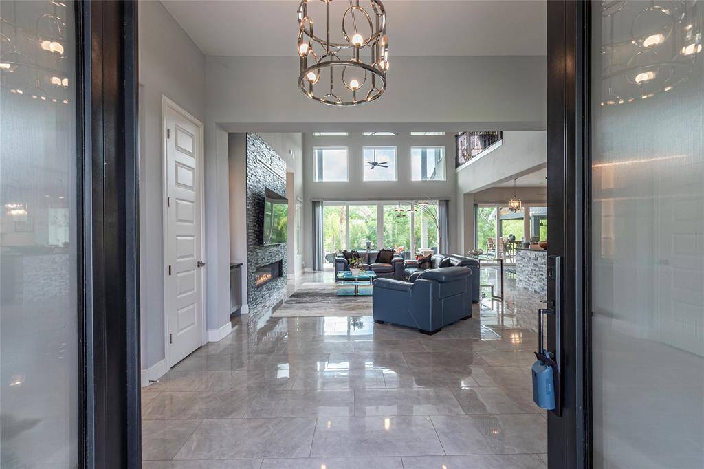 An inviting entryway featuring custom reinforced metal and double glass doors welcomes you into the opulent interior, where exquisite tile flooring and a dramatic hanging light fixture set the tone for luxury living.