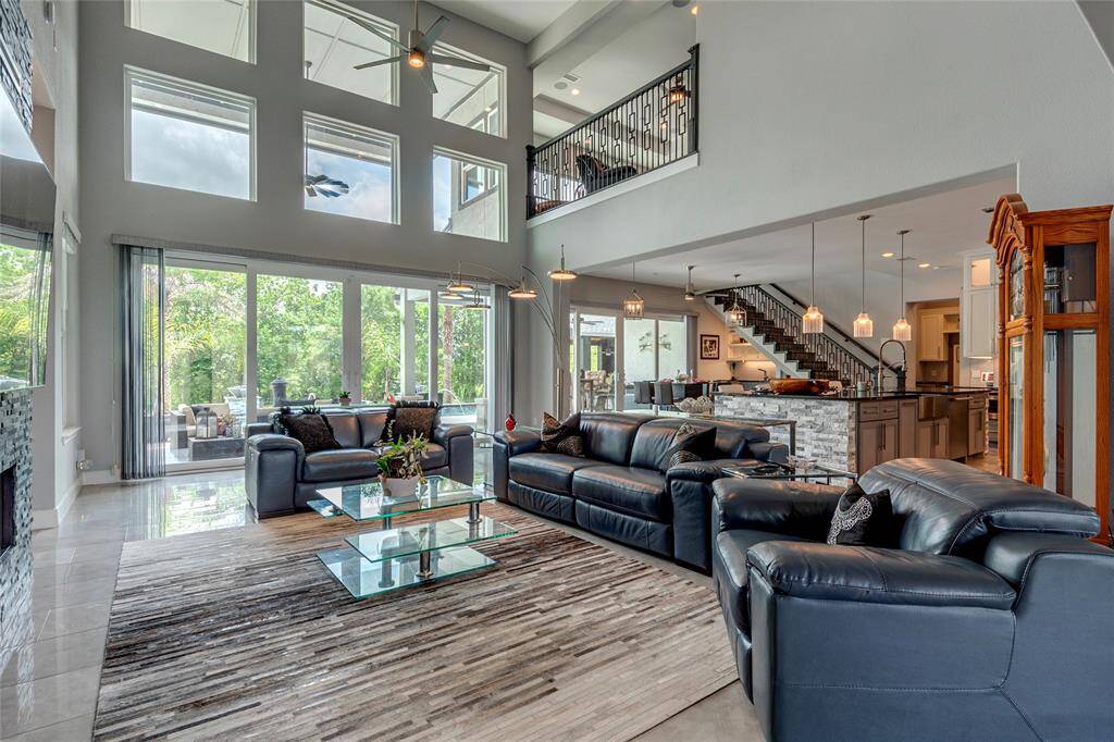 Grand living room spanning two levels with 18-foot ceilings offers striking pool and patio views; storm-proof sliding glass doors provide direct access to the outdoor living space; this designer layout flows seamlessly into the kitchen and dining areas—ideal for both relaxation and entertaining.