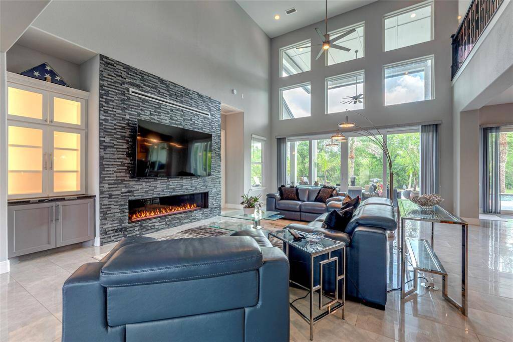 Dramatic living room showcasing tile flooring, soaring ceilings, and a custom stacked-stone glass accented fireplace flanked by built-in cabinetry with integrated accent lighting—where luxury and comfort converge.