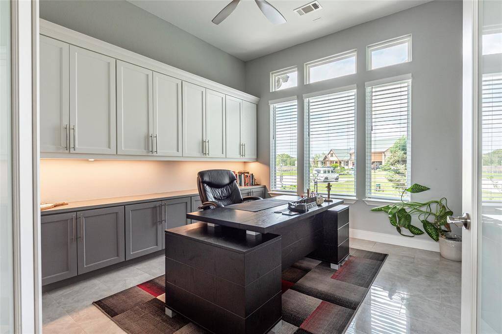 Private home office featuring double French doors, custom built-in soft-close storage cabinets with under-cabinet lighting, and front yard views—offering a comfortable and convenient work-from-home retreat.