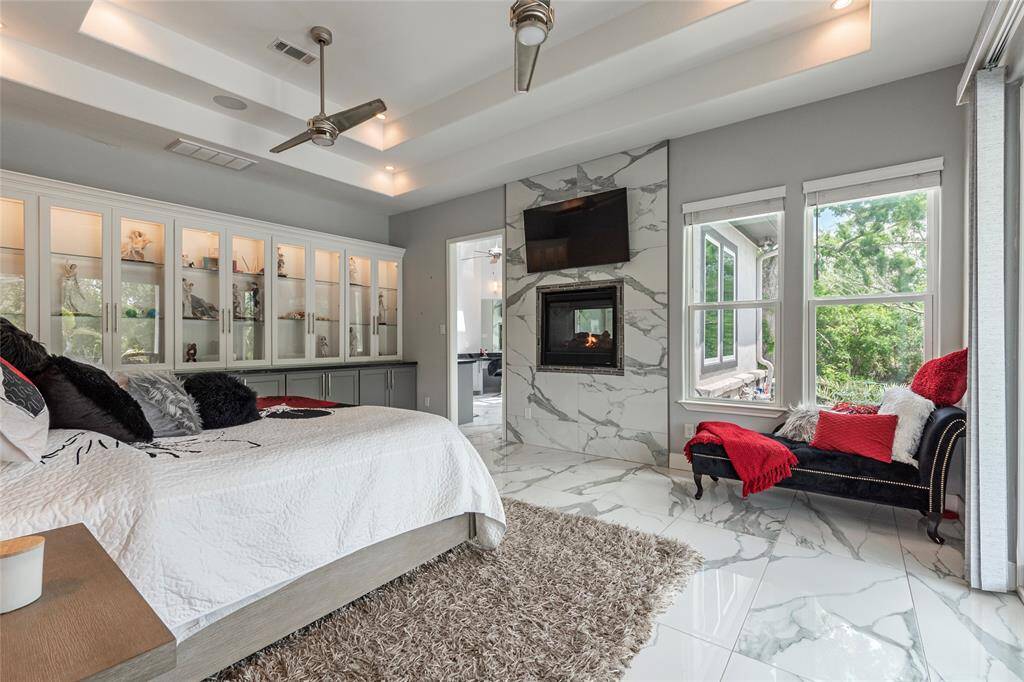 Sophisticated and sexy, the primary suite features a double-sided fireplace with granite surrounding, custom built-in cabinets with glass doors and accent lighting, double ceiling fans, and storm-proof sliding glass doors providing direct access to the outdoor oasis with hot tub, pool, and patio - a private resort-style escape.