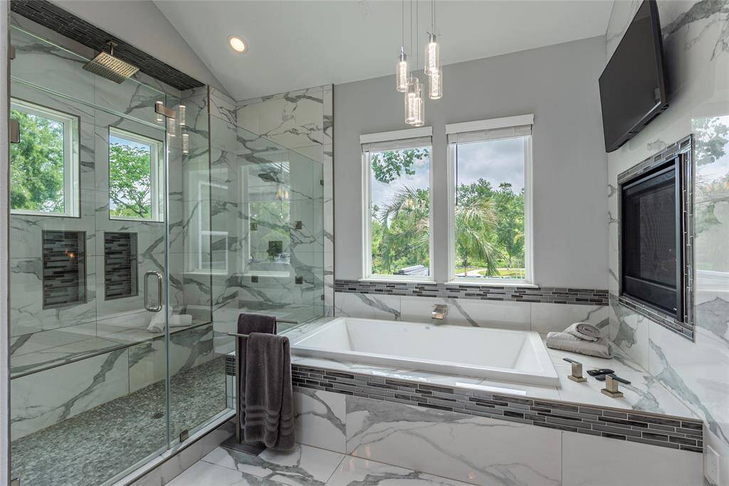 Indulge in the lavish 9-foot walk-in shower with a 6-foot seating bench, beautifully flanked by a 72" x 42" bubble tub. A sexy double-sided fireplace and stunning tile work with glass accents create a spa-like sanctuary infused with warmth and style, while providing serene backyard views.