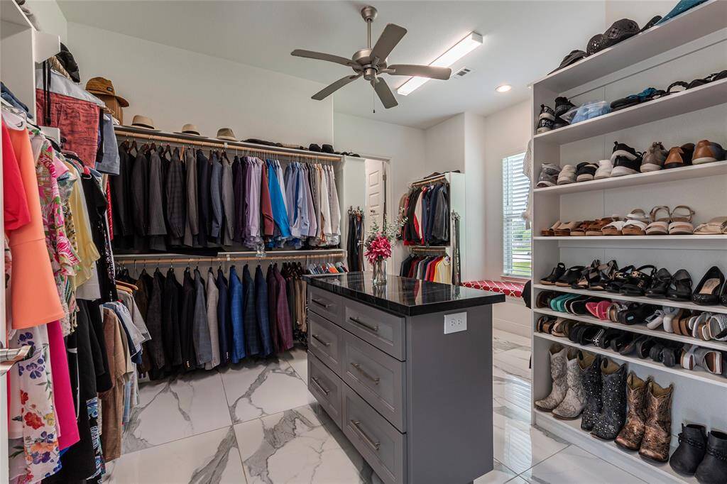 Stunning 16' x 14' walk-through wardrobe features a granite-topped built-in dresser and folding table, ceiling shelving, and a cozy bench beneath the window for seating comfort. Enjoy the ultimate in convenience with direct access from the primary closet into the utility room—combining elegance with everyday functionality.