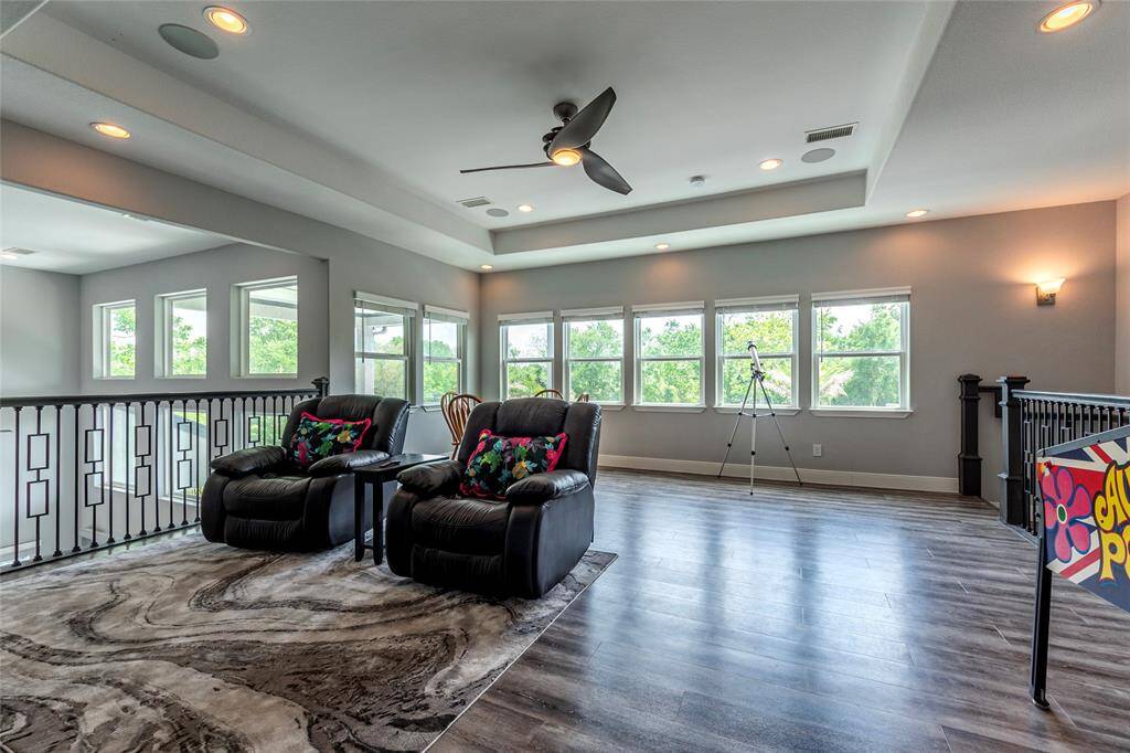 The upstairs game/media room boasts luxury vinyl flooring, a wet bar, and high ceilings, opening to the living room below with pool and pond views—perfect for entertainment and relaxation.